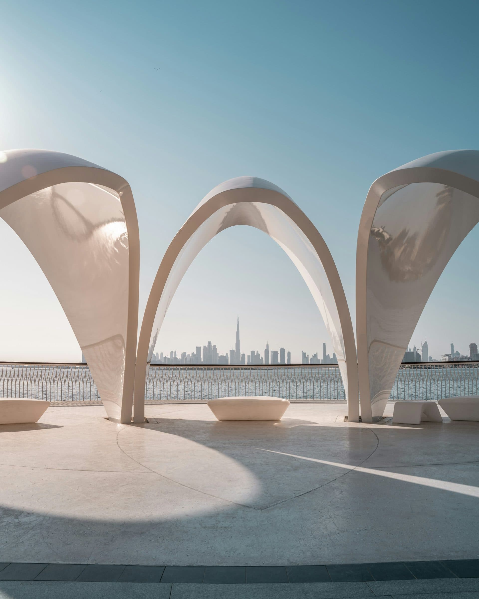 White arches at a Dubai waterfront with the city skyline beyond